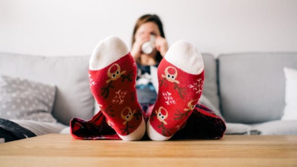 After saving money for Christmas, a woman relaxes with her feet up in reindeer socks, sipping hot chocolate.