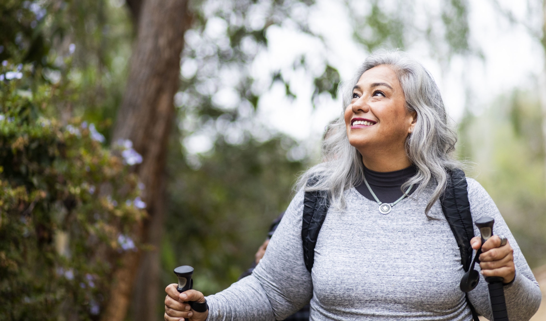 Smiling mature woman with gray hair hiking in a forest, symbolizing the balance between financial and mental health, as promoted by Money Mentors in helping manage debt.