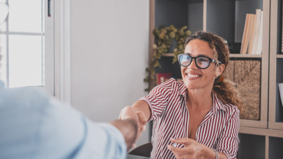 a smiling woman with glasses shakes a Money Mentors manager's hand after being hired.
