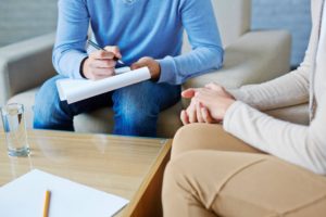 Counsellor with a clipboard in a blue jumper takes notes.