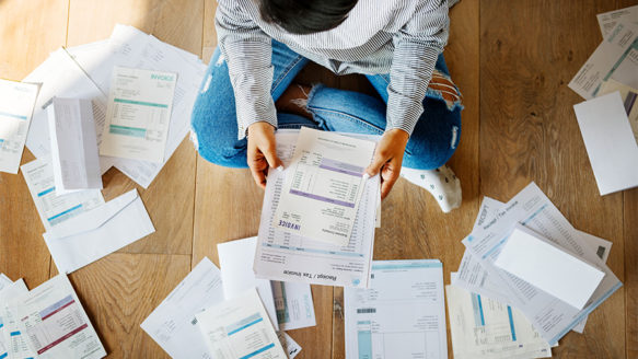 A woman surrounded by bills and invoices on the floor, looking stressed while managing personal finances—illustrating the emotional toll of credit card debt.