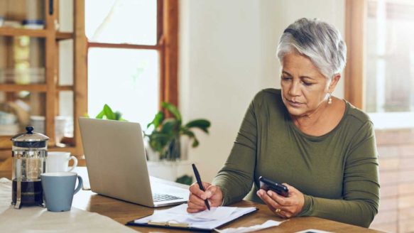 Middle-aged woman at dining table calculates her debts to evaluate pros and cons of bankruptcy vs OPD