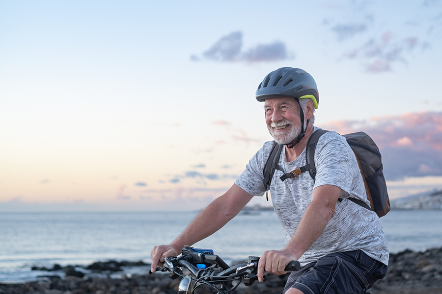 An older man on a bicycle cycles along the coast, smiling after his new found financial freedom.