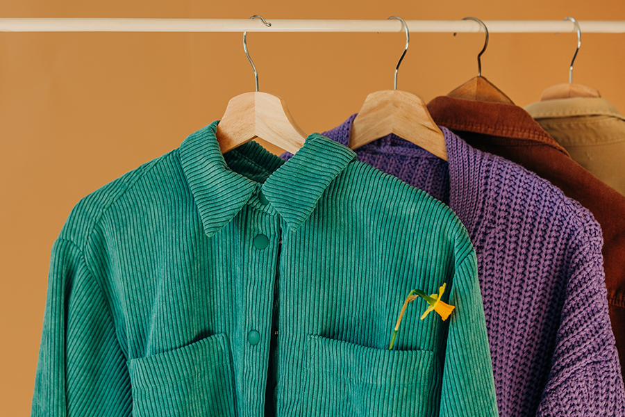 Colorful clothes hanging on wooden hangers; save money on stylish clothing with budgeting advice from Money Mentors.