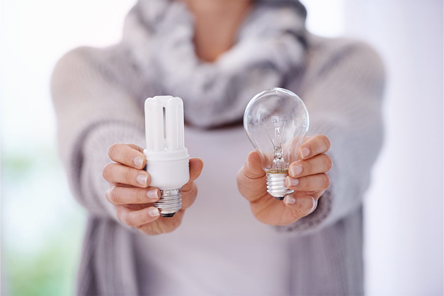 Person holding an LED bulb and an incandescent bulb; save money on electricity with energy-saving tips from Money Mentors.