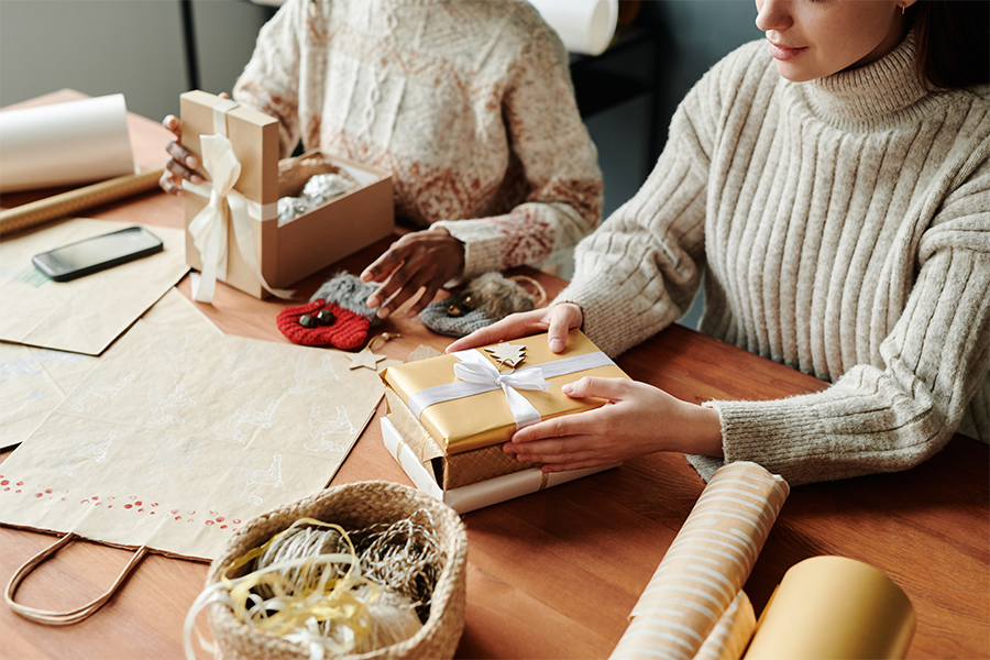 Two people wrapping gifts with ribbon and paper; save money on presents with budgeting tips from Money Mentors.