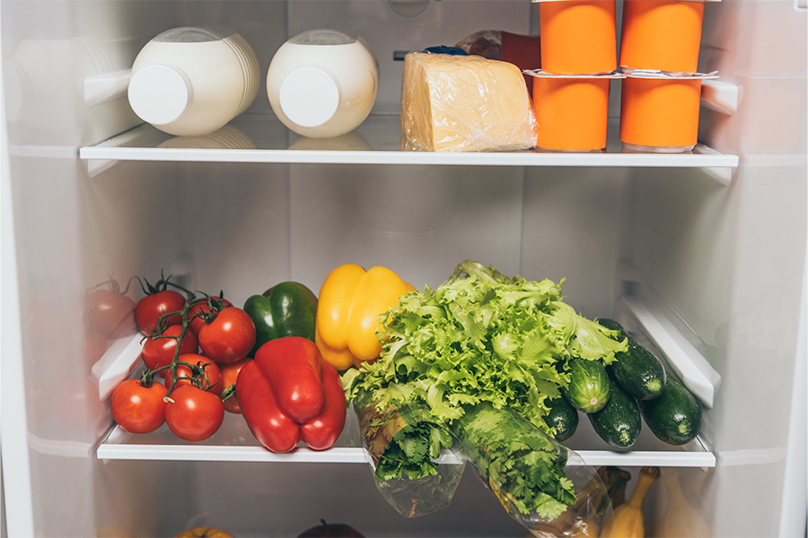 A refrigerator stocked with fresh vegetables, dairy products, and cheese; save money on groceries with budgeting tips from Money Mentors.