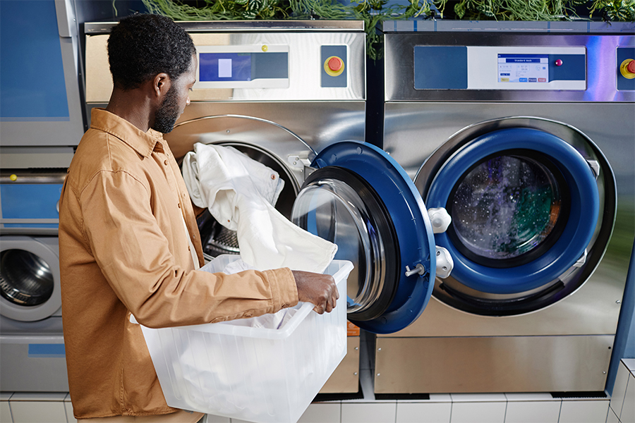 A man using a washing machine in a laundromat; save money on laundry expenses with financial tips from Money Mentors.