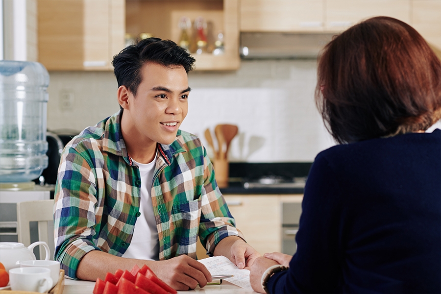 A young male student discusses his student loan with his mother. 