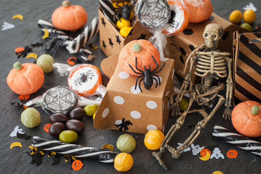 Assortment of affordable Halloween treats and decorations, including candy, decorative boxes, and a miniature skeleton, aligning with cost-saving tips from the 'How to Save Money at Halloween' blog post by Money Mentors.