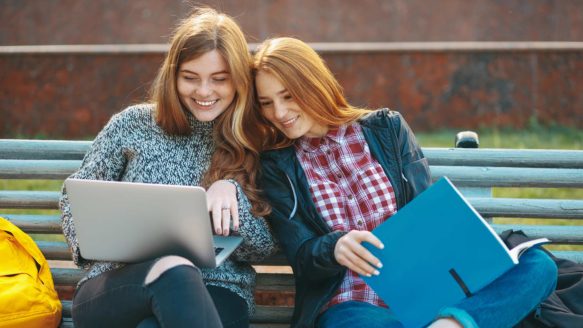 Two female high school students play Conquer Cashalot on their laptops to practice budgeting skills