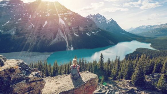 A young woman is sitting on a large rock overlooking a turquoise lake, debt free and planning her future