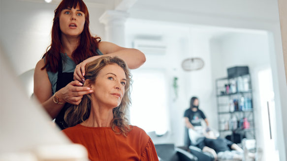 A hairstylist helping a client in a salon, representing small business owners managing money and reducing financial stress.