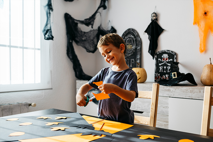 Young boy joyfully crafting Halloween decorations at home, showcasing DIY savings strategies as advised in the 'How to Save Money at Halloween' blog post by Money Mentors.