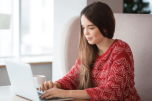 A woman in a red shirt works on her budget at the computer to build good spending habits