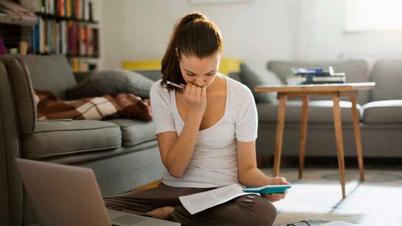 Young adult sitting on living room floor budgeting to save money