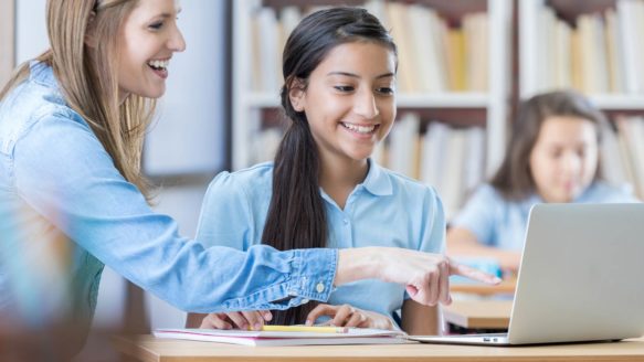A high school teacher helps a teenage girl with a Money Mentors school program on the computer