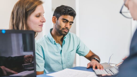 A couple sits at a table reviewing a document with a financial counsellor.