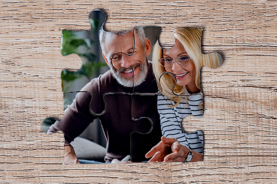 An image of a jigsaw puzzle on a wooden surface. The puzzle depicts a smiling elderly couple, symbolizing the concept that debt consolidation, much like a puzzle, involves bringing different pieces together to complete the picture. This can be associated with the services provided by Money Mentors, who help in organizing various debts into a single, manageable solution.
